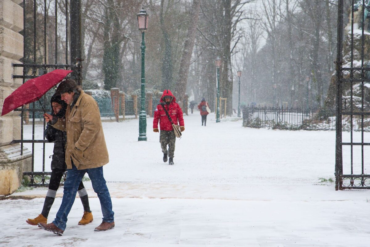 People walking huddling together under an umbrella in the snow in Via Garibaldi.