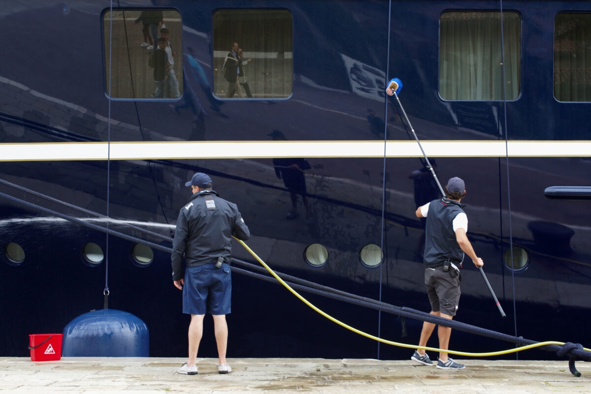 Two sailors occupied with maintenance and cleaning work on a yacht moored in Riva dei 7 martiri in Venice, Italy.